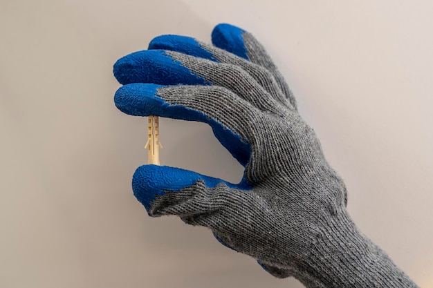 Die Hand eines Arbeiters 39 in einem Schutzhandschuh hält einen Plastikdübelstift