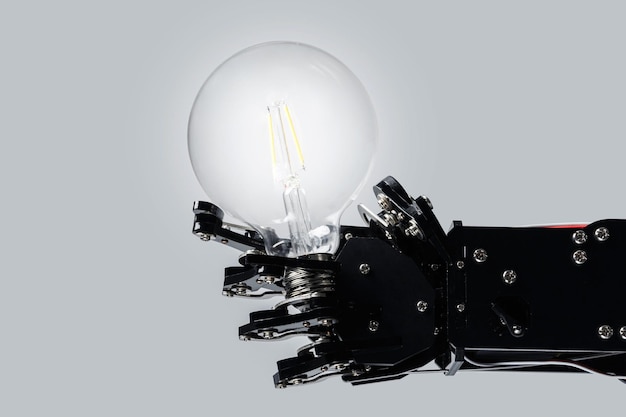 Die Hand eines echten Roboters hält eine Glühbirne auf grauem Hintergrund. Konzepte der Entwicklung künstlicher Intelligenz und des maschinellen Lernens