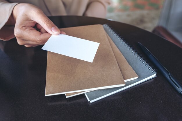 Foto die hand eines geschäftsmannes, die leere visitenkarte mit notizbüchern auf tisch hält und gibt