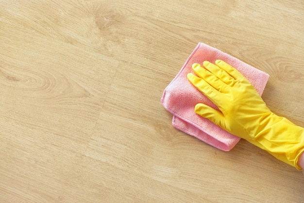 Die Hand eines Mannes gelbes Gummihandschuhöl poliert die Holzoberfläche Tisch der Boden rosa Lappen Reinigung