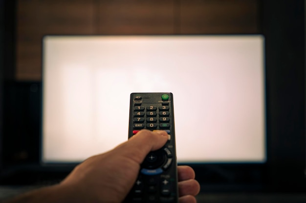 Die Hand eines Mannes hält die Fernbedienung vor einem großen weißen Fernsehbildschirm, verschwommene Fernbedienung für das Fernsehen