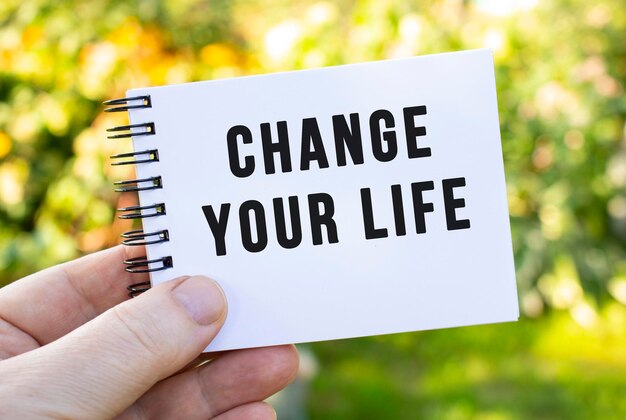 Foto die hand eines mannes hält ein notizbuch mit der aufschrift change your life notepad auf dem hintergrund der natur