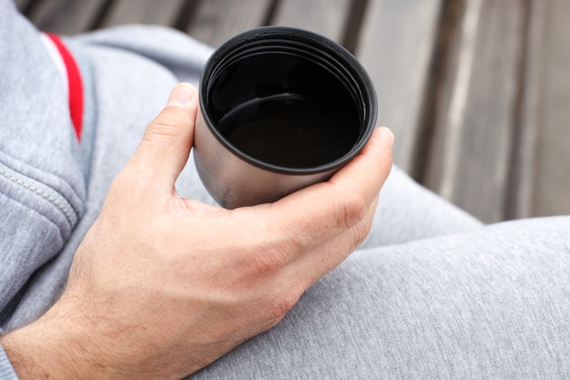 Die Hand eines Mannes hält eine Tasse Tee oder Kaffee aus einer Thermoskanne.