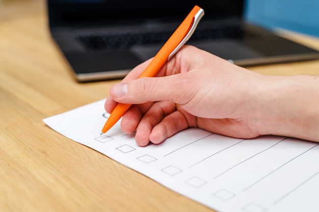 Die Hand eines Mannes hält einen Stift und schreibt eine Checkliste mit Kontrollkästchen, einen Holztisch