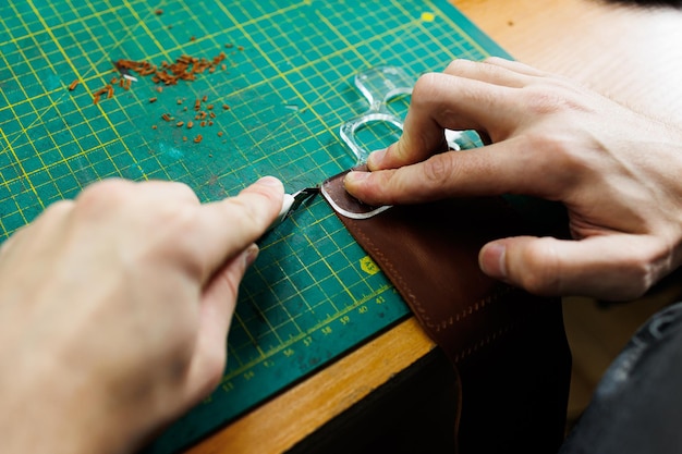Die Hand eines Mannes hält Lederstücke für eine Ledergeldbörse in seiner Werkstatt Der Prozess der Arbeit mit natürlichem braunem Leder Der Handwerker hält das Handwerk