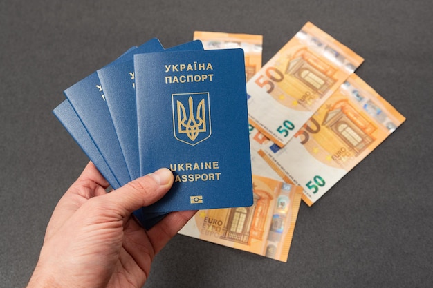 Die Hand eines Mannes hält vier ukrainische Pässe auf Bargeld-Euro-Hintergrund. Erlangung und Umtausch ausländischer Pässe