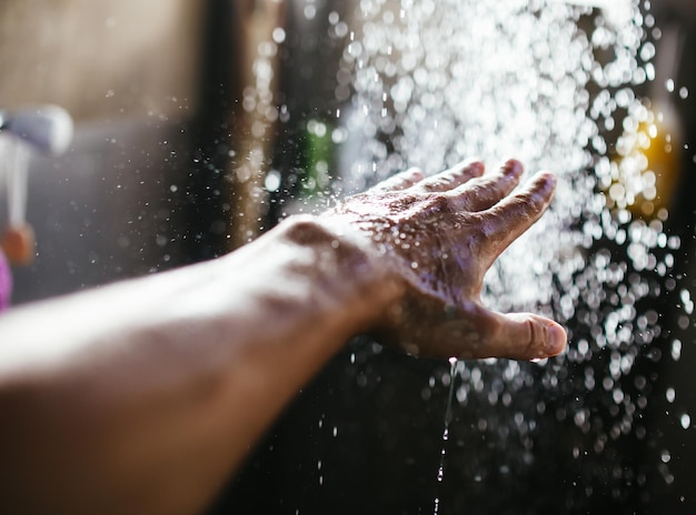 Die Hand eines Mannes in einem Wasserstrahl im Sonnenlicht vor einem dunklen Hintergrund.