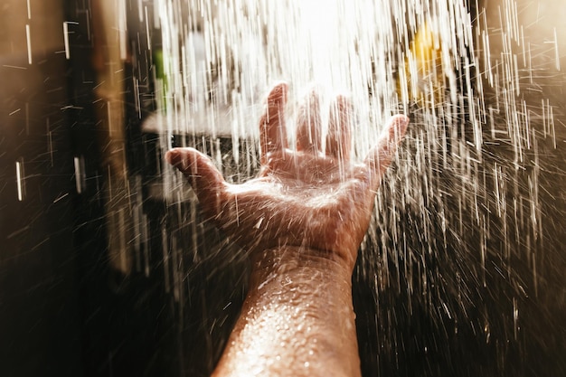 Die Hand eines Mannes in einem Wasserstrahl im Sonnenlicht vor einem dunklen Hintergrund.