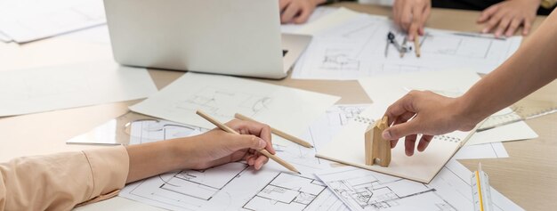 Die Hand eines professionellen Architekten zeichnet einen Entwurf auf einem Tisch mit einem Architekturdokument und Holzklötzen, die im Büro herumliegen. Design- und Planungskonzept. Fokus auf die Handzeichnung. Nahaufnahme