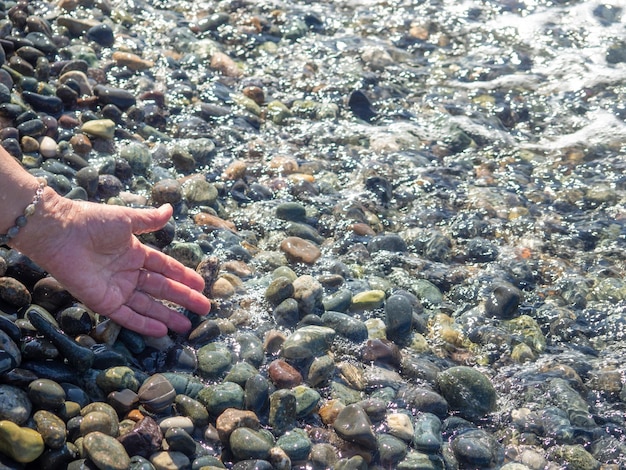 Die Hand greift nach dem Wasser. Meereswelle und weibliche Hand spüren die Welle. Kieselstrand