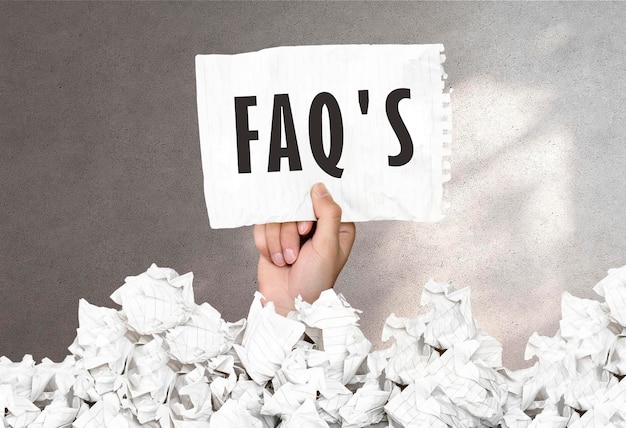 Die Hand hält ein Blatt Papier mit dem Text „FAQ'S“ auf einem grauen Wandhintergrund