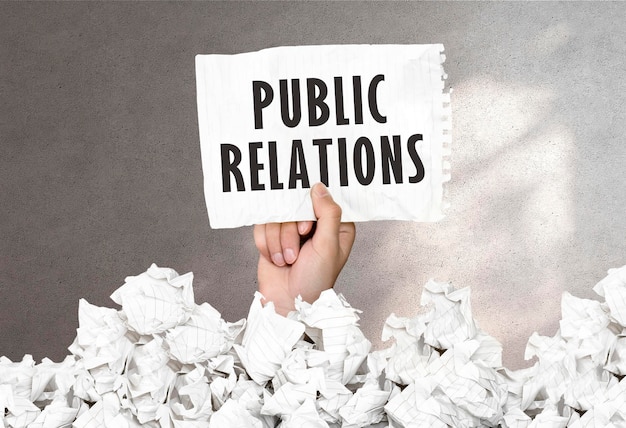 Foto die hand hält ein blatt papier mit dem text „public relations“ auf einem grauen wandhintergrund