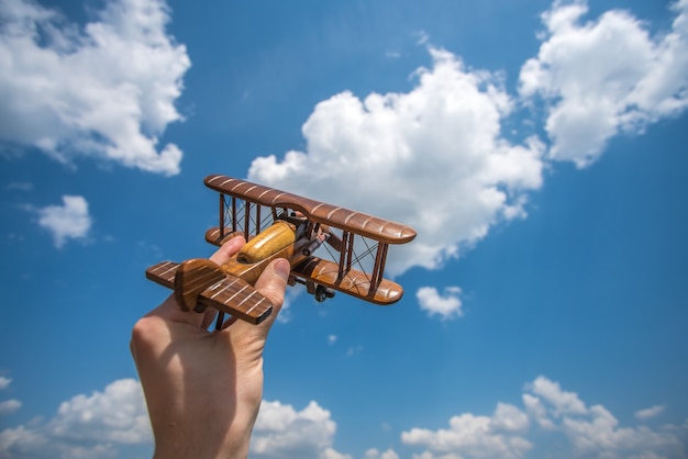 Die Hand hält ein Spielzeugflugzeug auf dem Hintergrund der Wolke