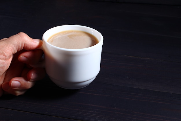 Die Hand hält eine Tasse Cappuccino auf einem dunklen