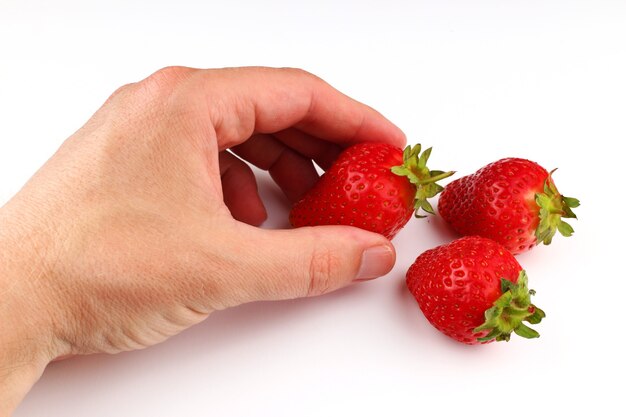 Die Hand hält Erdbeeren auf einer weißen Oberfläche