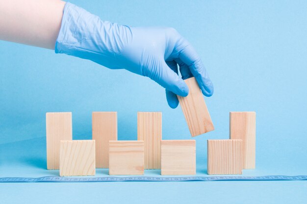 Die Hand in einem blauen medizinischen Einweghandschuh aus Gummi nimmt einen Dominoblock