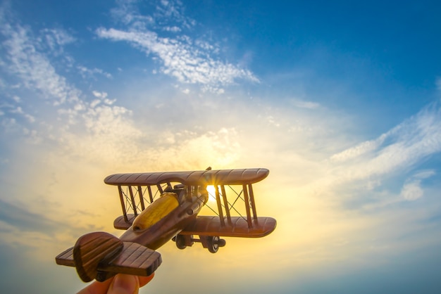 Die Hand mit einem Holzflugzeug auf dem Hintergrund des Sonnenuntergangs