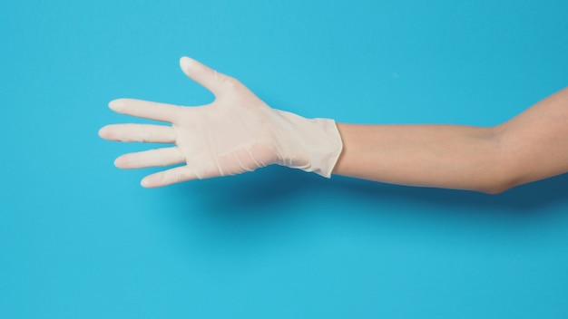 Die Hand trägt weiße OP-Handschuhe oder Latexhandschuhe auf blauem oder türkisfarbenem Hintergrund.