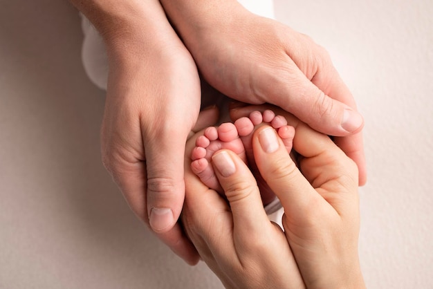 Die Handflächen der Eltern Ein Vater und eine Mutter halten die Füße eines Neugeborenen in einer weißen Decke auf weißem Hintergrund Die Füße eines Neugeborenen in den Händen der Eltern Foto von Fußabsätzen und Zehen