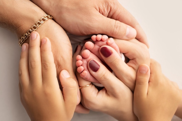 Die Handflächen der Eltern Ein Vater und eine Mutter halten die Füße eines neugeborenen Kindes auf einem weißen Studiohintergrund Die Füße eines Neugeborenen in den Händen der Eltern Makrofotografie von Fußabsätzen und Zehen