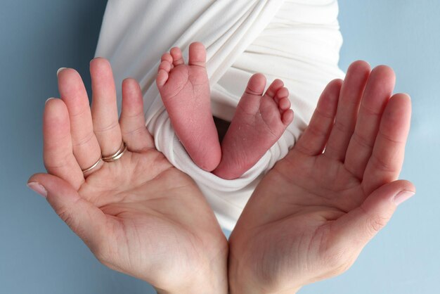 Die Handflächen der Eltern, Vater und Mutter, halten die Beine, die Füße eines Neugeborenen in einer weißen Hülle auf blauem Hintergrund, Füße, Fersen, Fersen und Zehen eines Neuborenen, professionelles Makrofoto