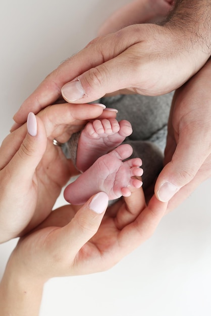 Die Handflächen des Vaters der Mutter halten den Fuß des neugeborenen Babys auf weißem Hintergrund Füße des Neugeborenen auf den Handflächen der Eltern Fotografie der Zehen, Fersen und Füße eines Kindes