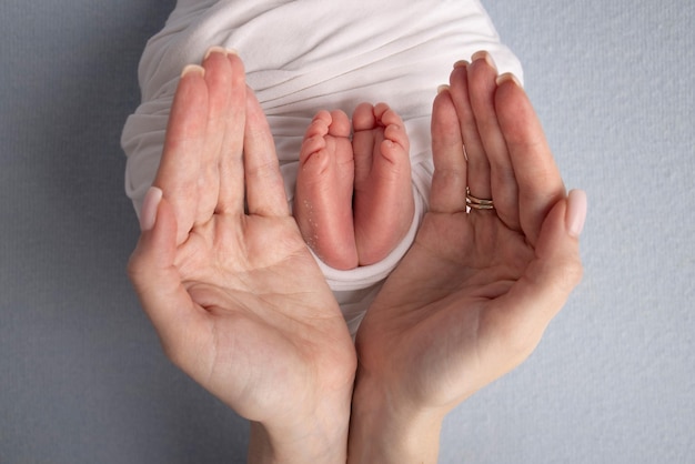 Die Handflächen des Vaters die Mutter hält den Fuß des Neugeborenen in einer weißen Decke Füße des Neugeborenen auf den Handflächen der Eltern Fotografie der Zehen, Fersen und Füße eines Kindes