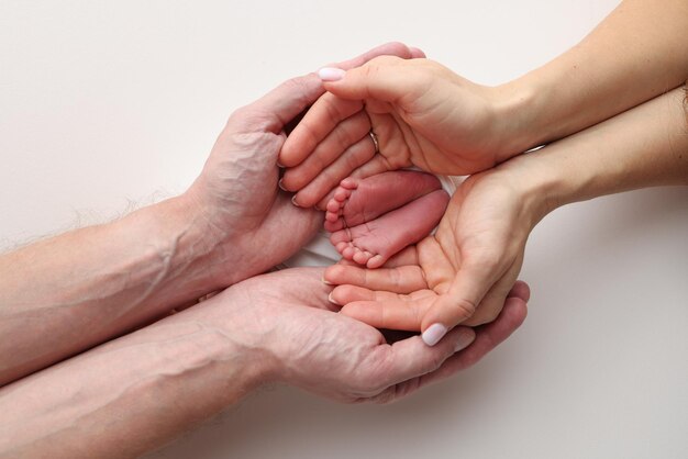 Die Handflächen des Vaters die Mutter halten den Fuß des neugeborenen Babys in einer weißen Decke Füße des Neugeborenen auf den Handflächen der Eltern Studio-Makrofoto eines Kindes Zehen Fersen und Füße