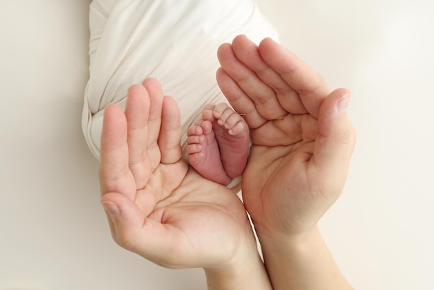 Die Handflächen des Vaters die Mutter halten den Fuß des neugeborenen Babys in einer weißen Decke Füße des Neugeborenen auf den Handflächen der Eltern Studio-Makrofoto eines Kindes Zehen Fersen und Füße