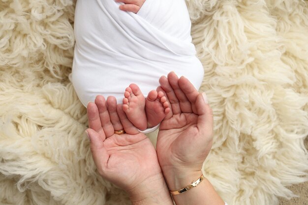 Die Handflächen des Vaters die Mutter halten den Fuß des neugeborenen Babys in einer weißen Decke Füße des Neugeborenen auf den Handflächen der Eltern Studio-Makrofoto eines Kindes Zehen Fersen und Füße