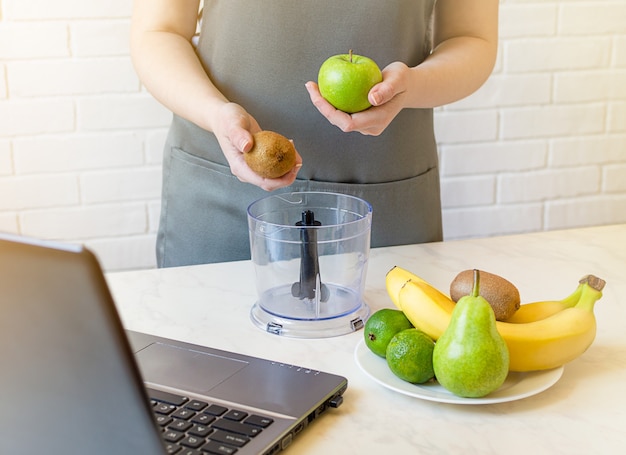 Die Hausfrau benutzt einen Laptop und bereitet frische Fruchtsmoothies zu.