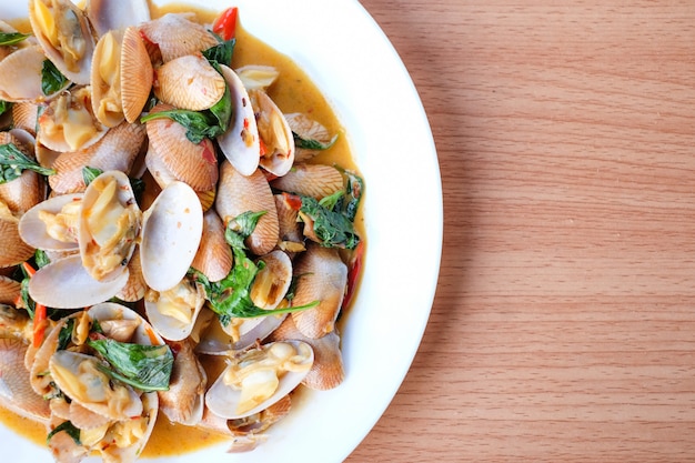 Foto die heißen gebratenen muscheln mit gerösteter chilipaste und basilikum servieren auf einem weißen teller auf einem braunen tisch - hausgemachtes lebensmittelkonzept.