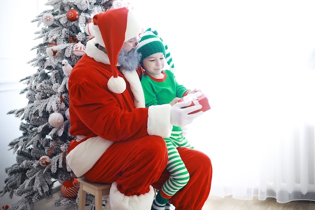 Die Helfer des Weihnachtsmanns. Süße Kinder in Weihnachtselfenkostümen in einem weihnachtlich dekorierten Raum. Zeit der Wunder. Geschenke vom Weihnachtsmann.