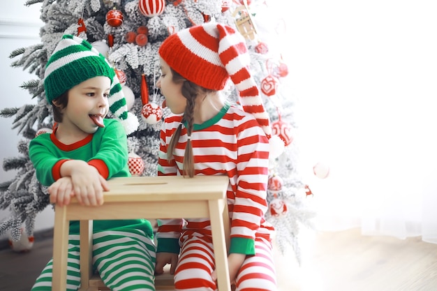 Die Helfer des Weihnachtsmanns. Süße Kinder in Weihnachtselfenkostümen in einem weihnachtlich dekorierten Raum. Zeit der Wunder. Geschenke vom Weihnachtsmann.