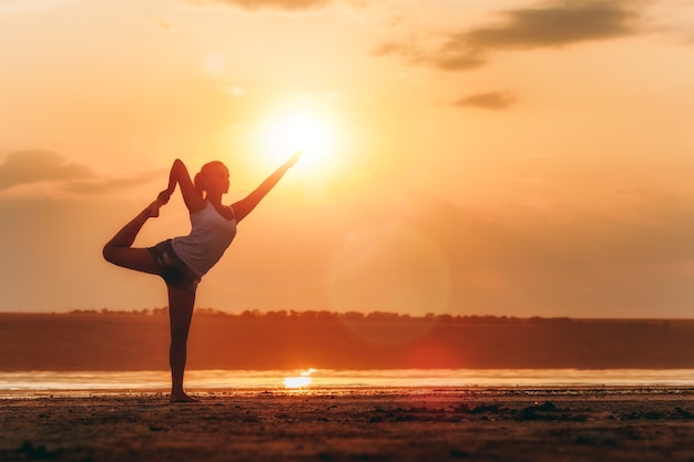 Die hübsche Frau macht Yoga bei Sonnenuntergang im Freien