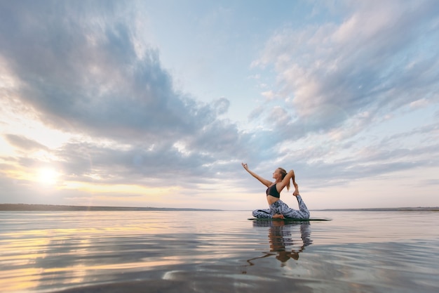 Die hübsche Frau macht Yoga bei Sonnenuntergang im Freien