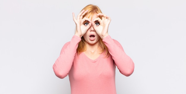 Foto die hübsche frau mit dem roten kopf fühlte sich schockiert, erstaunt und überrascht und hielt eine brille mit einem erstaunten, ungläubigen blick