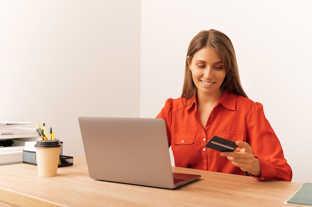 Foto die im büro arbeitende frau nutzt internet-banking und hält eine kreditkarte