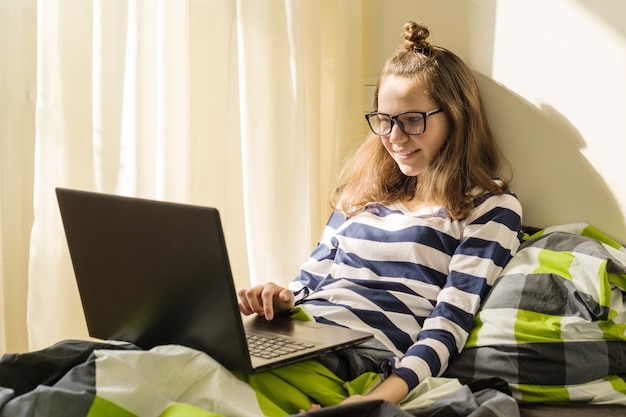 Die Jugendliche, die zu Hause studiert, benutzt Laptop im Bett