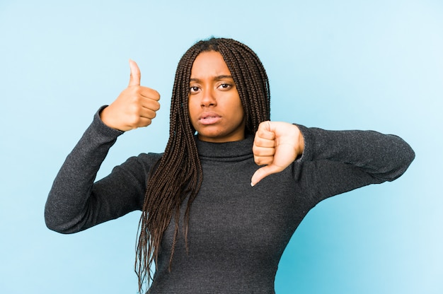 Die junge Afroamerikanerfrau, die auf der blauen Wand zeigt Daumen hoch und Daumen unten, schwierig lokalisiert wird, wählen Konzept