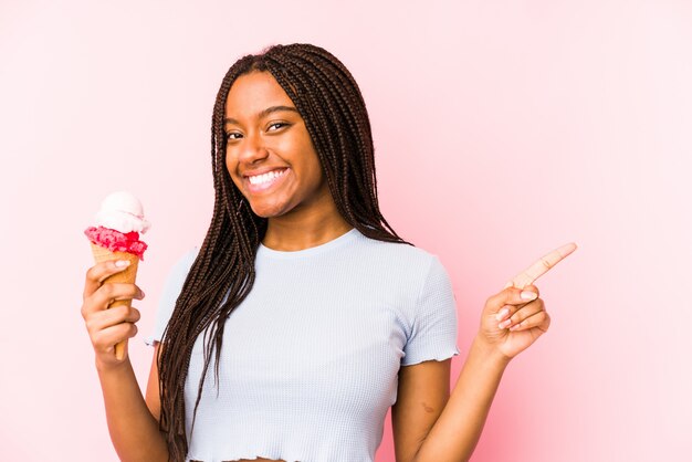 Die junge Afroamerikanerfrau, die eine Eiscreme hält, lokalisierte das Lächeln und beiseite zeigen und zeigte etwas auf Leerstelle.