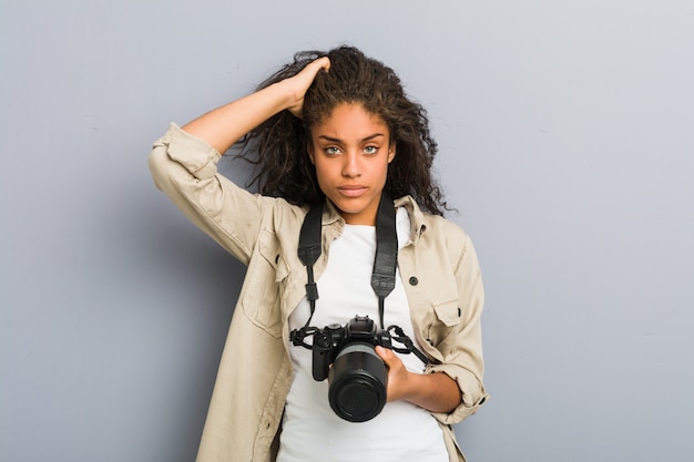 Die junge Afroamerikanerphotographfrau, die eine Kamera entsetzt hält, hat sich an wichtige Sitzung erinnert.