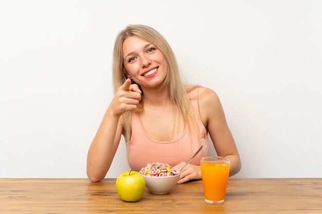 Die junge blonde Frau, die frühstückt, zeigt Finger auf Sie