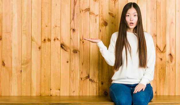 Die junge chinesische Frau, die auf einem hölzernen Platz sitzt, beeindruckte das Halten des Kopienraumes auf Palme.