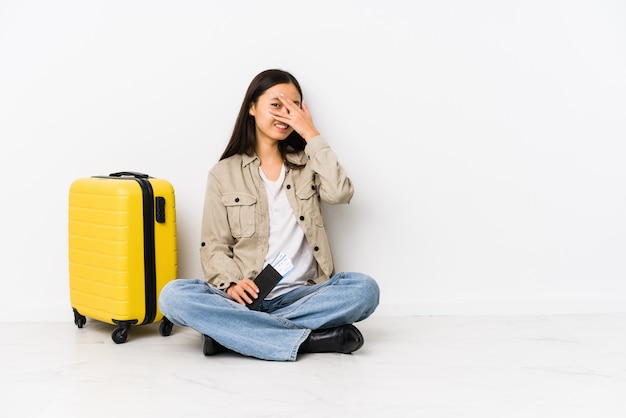 Die junge chinesische Reisendfrau, die eine Bordkarte halten sitzt, blinken durch verlegenes Bedeckungsgesicht der Finger an.