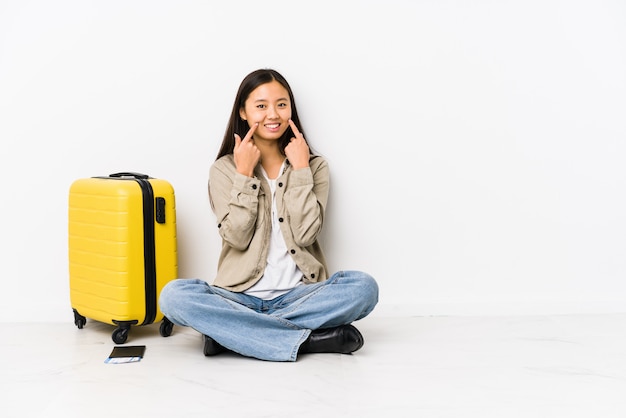 Die junge chinesische Reisendfrau, die eine Bordkarte halten sitzt, lächelt und zeigt Finger auf Mund.