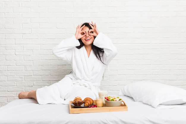 Die junge curvy Frau, die ein Frühstück auf dem Bett zeigt okay nimmt, unterzeichnen vorbei Augen