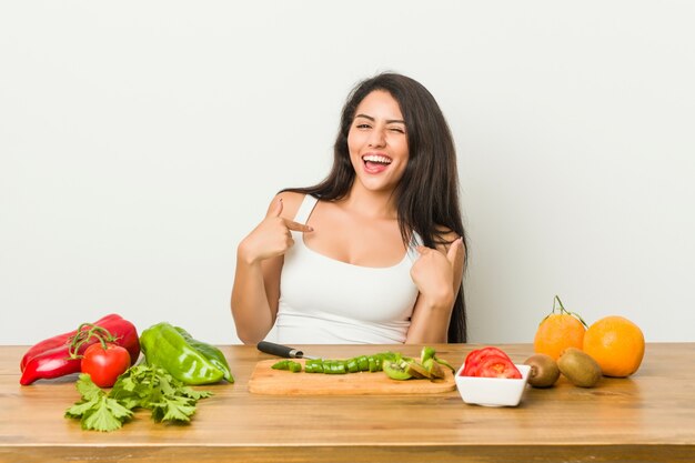 Die junge curvy Frau, die eine gesunde Mahlzeit vorbereitet, überraschte das Zeigen mit dem Finger und breit lächelte.