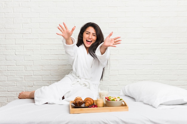 Die junge Frau, die auf dem Bett frühstückt, fühlt sich überzeugt, der Kamera eine Umarmung zu geben.