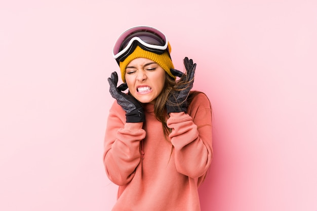 Die junge Frau, die einen Ski trägt, kleidet lokalisierte Bedeckungsohren mit den Händen.